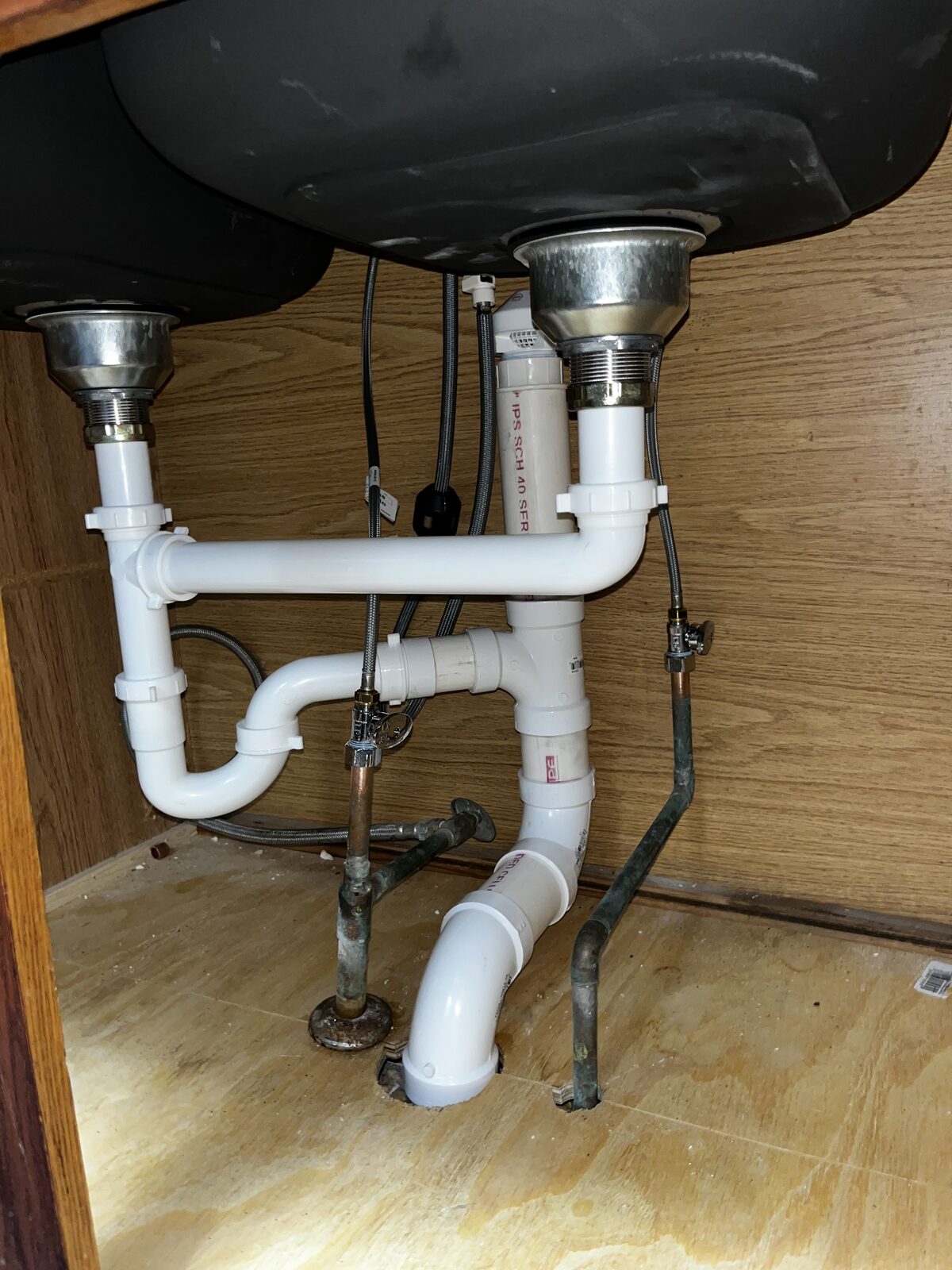 Rebuilt double-bowl kitchen sink drain with new PVC trap assembly and supply connections under the cabinet
