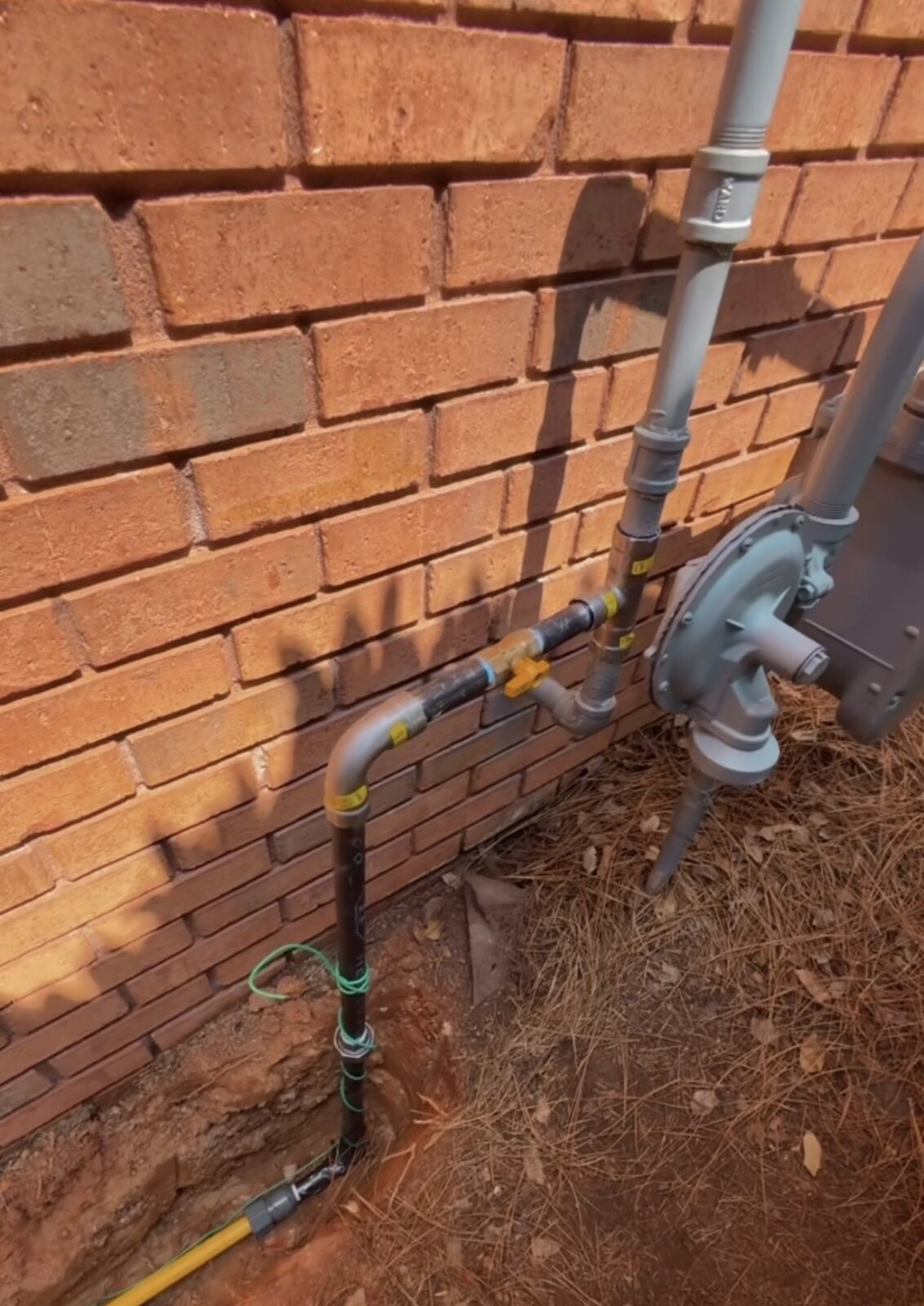 New coated gas line run along a brick exterior wall tied into the meter and regulator with a shutoff valve